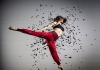 A woman wearing red trousers, mid leap, surrounded by swirling black confetti A woman wearing red trousers, mid leap, surrounded by swirling black confetti