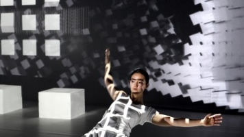 A dancer on their knees with black and white square projections all over the stage A dancer on their knees with black and white square projections all over the stage