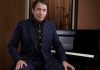 Band leader Jools Holland sits at a black Yamaha piano, wearing a dark blue pin-striped suit. Band leader Jools Holland sits at a black Yamaha piano, wearing a dark blue pin-striped suit.