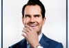 Jimmy Carr laughs into his hand whilst looking to the side, wearing a navy suit and a patterned tie. Jimmy Carr laughs into his hand whilst looking to the side, wearing a navy suit and a patterned tie.