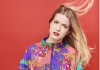 Olga Koch, a woman with long blonde hair that is blowing to one side, wearing a brightly coloured bomber jacket Olga Koch, a woman with long blonde hair that is blowing to one side, wearing a brightly coloured bomber jacket