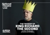 A man in a dark grey t-shirt with a large yellow paper crown on his head A man in a dark grey t-shirt with a large yellow paper crown on his head
