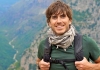 Adventurer Simon Reeves stands in front of a green valley, wearing a green t shirt and a backpack Adventurer Simon Reeves stands in front of a green valley, wearing a green t shirt and a backpack