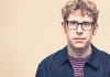 Comedian Josh Widdicombe stares at the camera, wearing a blue jacket and striped top. Comedian Josh Widdicombe stares at the camera, wearing a blue jacket and striped top.