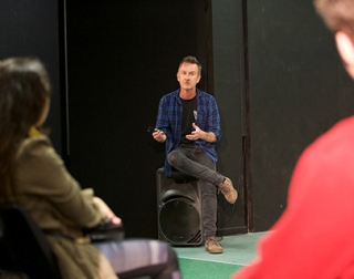 Chris O'Connell, the class teacher, sits on a speaker talking to students. He is wearing a blue checked shirt over a black tee shirt Chris O'Connell, the class teacher, sits on a speaker talking to students. He is wearing a blue checked shirt over a black tee shirt