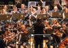An orchestra, with a conductor, stood with her back to us An orchestra, with a conductor, stood with her back to us