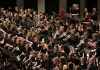 Students are sat in an orchestra, holding brass instruments. Students are sat in an orchestra, holding brass instruments.