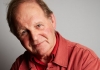 Author Michael Morpurgo sits against a grey background, wearing an orange shirt and looking at the camera. Author Michael Morpurgo sits against a grey background, wearing an orange shirt and looking at the camera.