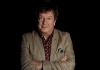 Stuart Maconie stands against a black background with his arms crossed wearing a checked suit Stuart Maconie stands against a black background with his arms crossed wearing a checked suit