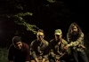 The four members of Turin Brakes in outdoors clothing sitting in the forest The four members of Turin Brakes in outdoors clothing sitting in the forest