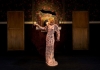 A blonde woman with short curly hair is acting in a long and floaty pink dress with sequins all over it A blonde woman with short curly hair is acting in a long and floaty pink dress with sequins all over it