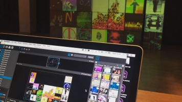 A laptop in the foreground with digital projections on the wall behind it. A laptop in the foreground with digital projections on the wall behind it.