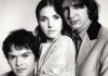 Black and white. Two men and a woman sit closely together, looking at the camera. Black and white. Two men and a woman sit closely together, looking at the camera.
