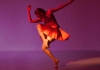 A dancer lit in red against a purple background. A dancer lit in red against a purple background.
