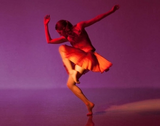 A dancer lit in red against a purple background. A dancer lit in red against a purple background.