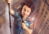 A man in a bright shirt hangs amongst high buildings, holding a microphone A man in a bright shirt hangs amongst high buildings, holding a microphone