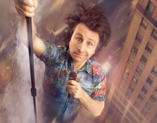 A man in a bright shirt hangs amongst high buildings, holding a microphone A man in a bright shirt hangs amongst high buildings, holding a microphone