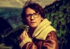 A man stands in front of a forest, wearing a leather jacket with a big collar, holding a flower A man stands in front of a forest, wearing a leather jacket with a big collar, holding a flower