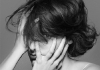 A woman looks at the camera with her hair and hands covering her face. Black and white. A woman looks at the camera with her hair and hands covering her face. Black and white.