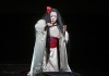 A woman dressed as a geisha in a long white robe with a red sash kneels on the floor, holding a knife between her hands A woman dressed as a geisha in a long white robe with a red sash kneels on the floor, holding a knife between her hands