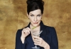 A woman with dark hair, wearing a jacket, holds a cocktail and smiles at the camera A woman with dark hair, wearing a jacket, holds a cocktail and smiles at the camera