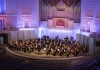 An orchestra plays in a opulent concert hall, lit with blue and purple lights An orchestra plays in a opulent concert hall, lit with blue and purple lights