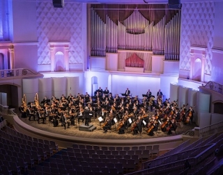 An orchestra plays in a opulent concert hall, lit with blue and purple lights An orchestra plays in a opulent concert hall, lit with blue and purple lights