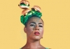 A person stands against a yellow background, wearing a hat and veil made of burgers as they look at the camera A person stands against a yellow background, wearing a hat and veil made of burgers as they look at the camera
