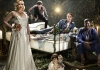 A bed in a forest, lit with fireflies and surrounded by performers. They include a blonde woman in a white dress, a young man balanced at the head of the bed, and a man in a purple shirt. A bed in a forest, lit with fireflies and surrounded by performers. They include a blonde woman in a white dress, a young man balanced at the head of the bed, and a man in a purple shirt.