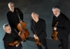 Four musicians dressed in black suits hold their instruments and look at the camera Four musicians dressed in black suits hold their instruments and look at the camera