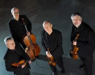 Four musicians dressed in black suits hold their instruments and look at the camera Four musicians dressed in black suits hold their instruments and look at the camera