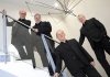Four men in black suits stand on a glass staircase, underneath a metal sculpture, and look at the camera Four men in black suits stand on a glass staircase, underneath a metal sculpture, and look at the camera