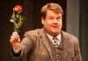 A man in a chequered brown suit holds out a rose A man in a chequered brown suit holds out a rose