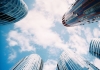 A photograph taken looking up to a blue sky, with cylindrical glass buildings all around A photograph taken looking up to a blue sky, with cylindrical glass buildings all around