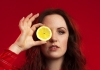 Woman looks at camera whilst holding a lemon over her eye Woman looks at camera whilst holding a lemon over her eye