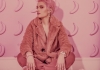 Woman with pink hair, dressed in pink coat, sits and looks at camera Woman with pink hair, dressed in pink coat, sits and looks at camera