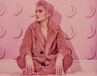Woman with pink hair, dressed in pink coat, sits and looks at camera Woman with pink hair, dressed in pink coat, sits and looks at camera