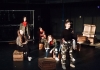 A group of young performers stand and sit on crates on a dark stage A group of young performers stand and sit on crates on a dark stage