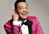 A man with dark hair, wearing a bright pink and black jacket, white shirt and black bow tie, smiles at the camera A man with dark hair, wearing a bright pink and black jacket, white shirt and black bow tie, smiles at the camera