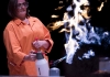 A woman in an orange science lab coat and protective goggles carrying out an experiment A woman in an orange science lab coat and protective goggles carrying out an experiment