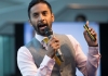 A man in a nice suit speaks into a microphone, raising his hand in the air A man in a nice suit speaks into a microphone, raising his hand in the air