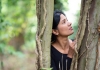 A South Asian woman standing between two trees and looking to the left. A South Asian woman standing between two trees and looking to the left.