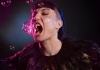 A woman wearing black feathers opening her mouth to eat pink bubbles A woman wearing black feathers opening her mouth to eat pink bubbles