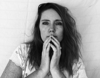 Black and white. A woman with long hair looks at the camera. Her hands are in front of her face. Black and white. A woman with long hair looks at the camera. Her hands are in front of her face.