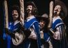 Four men with curly hair in blue coats, stood looking sideways at the camera and holding french baguettes. Four men with curly hair in blue coats, stood looking sideways at the camera and holding french baguettes.