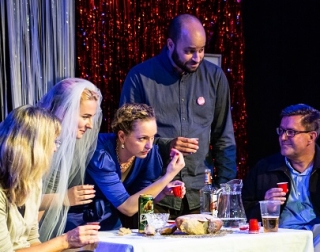 A group of people round a table holding shot glasses, one is wearing a wedding veil A group of people round a table holding shot glasses, one is wearing a wedding veil