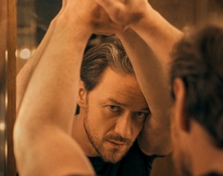 A man in a black t-shirt leaning on a mirror and looking at his reflection. A man in a black t-shirt leaning on a mirror and looking at his reflection.