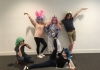A group of youth theatre performers pose for the camera, wearing colourful wigs. A group of youth theatre performers pose for the camera, wearing colourful wigs.