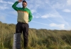 A Man wearing a baseball cap standing in long grass with his hand in the air and a keyboard resting on his leg A Man wearing a baseball cap standing in long grass with his hand in the air and a keyboard resting on his leg