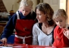 A woman and two girls wearing aprons sit and stand behing a table and make chocolate A woman and two girls wearing aprons sit and stand behing a table and make chocolate